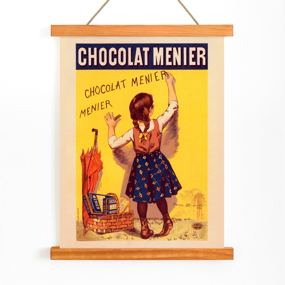 Chocolat Menier poster by Firmin Bouisset featuring a young girl writing on a yellow wall with a basket of chocolate and an umbrella, with wooden magnetic frame on white background