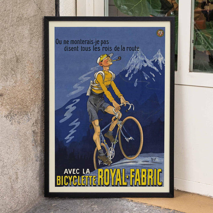 Michel Liebeaux Royal-Fabric bicycle poster with cyclist riding uphill in yellow gear against a moody blue mountain sky, framed and displayed in modern living room decor