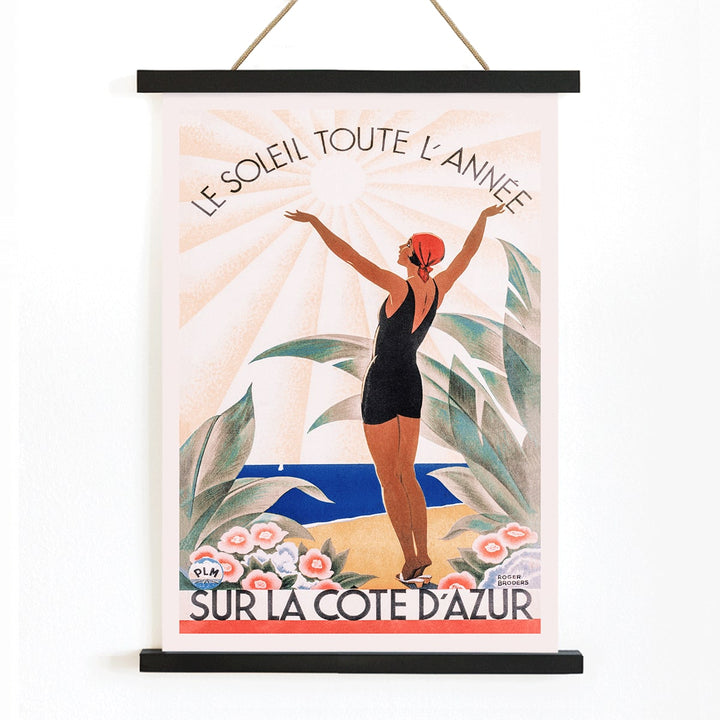 Woman in swimsuit enjoying sunny beach scenery surrounded by flowers Cote dAzur artwork by Roger Broders, with wooden magnetic frame on white background