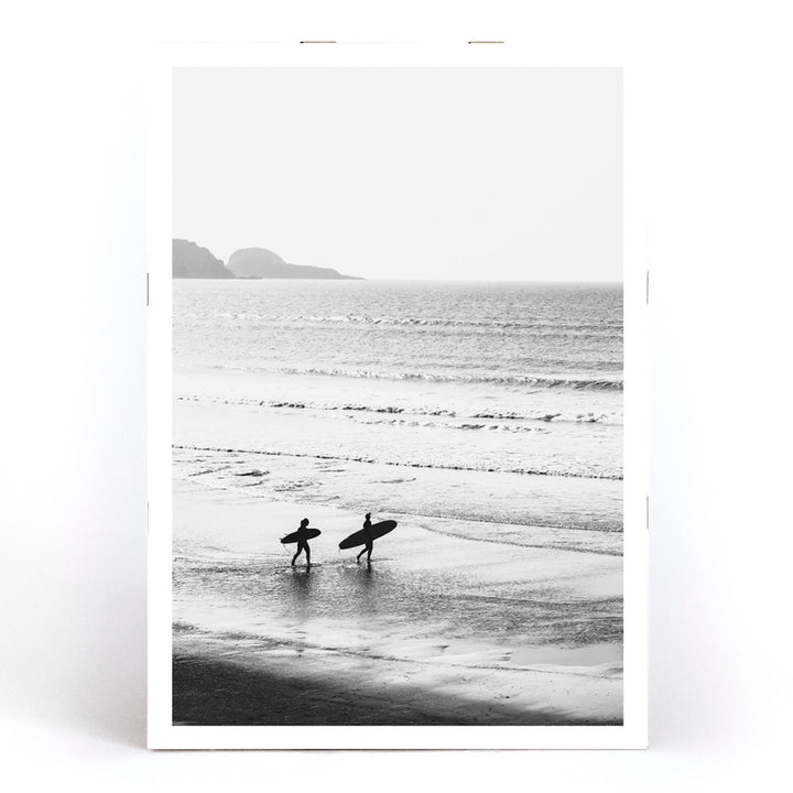 Black and white poster of surfers walking along the beach Surfers walking on the beach artwork, framed and displayed in modern living room decor